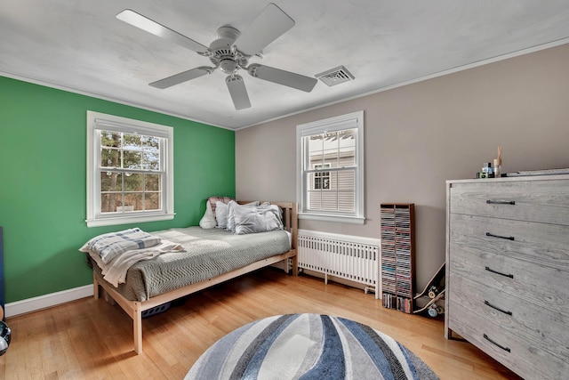 bedroom with multiple windows, visible vents, radiator heating unit, and wood finished floors