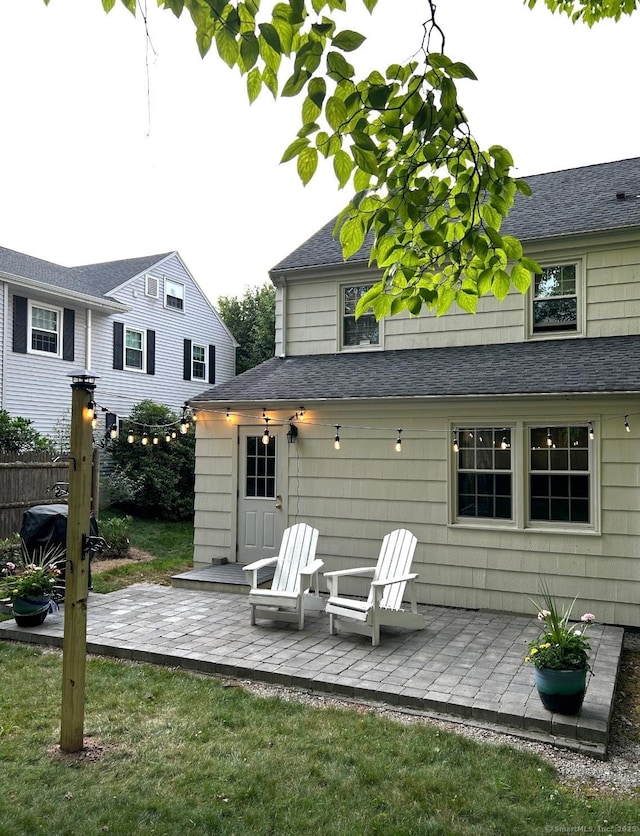 rear view of property featuring a shingled roof, a yard, a patio area, and fence