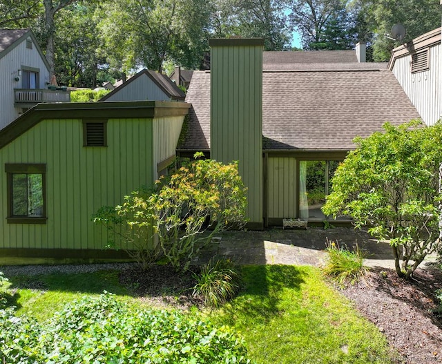 view of home's exterior featuring a lawn, a shingled roof, and a chimney