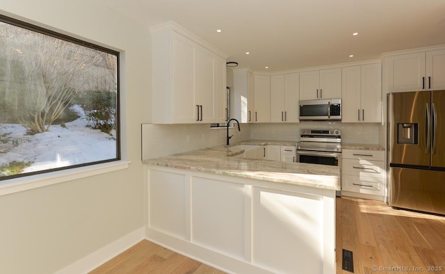 kitchen with light stone countertops, a sink, stainless steel appliances, light wood-type flooring, and white cabinets