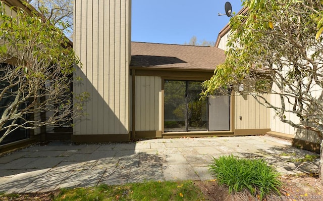 property entrance with a chimney, a patio area, and a shingled roof