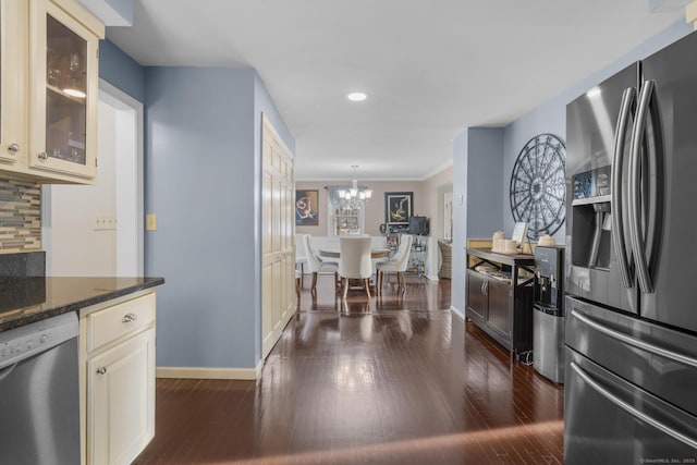 kitchen with appliances with stainless steel finishes, glass insert cabinets, cream cabinets, and tasteful backsplash