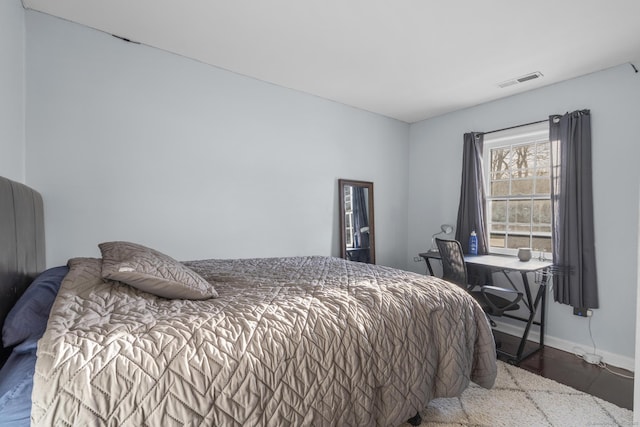 bedroom with baseboards, visible vents, and wood finished floors