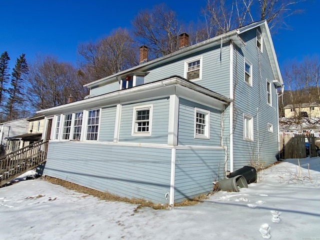 view of snowy exterior featuring a chimney and fence