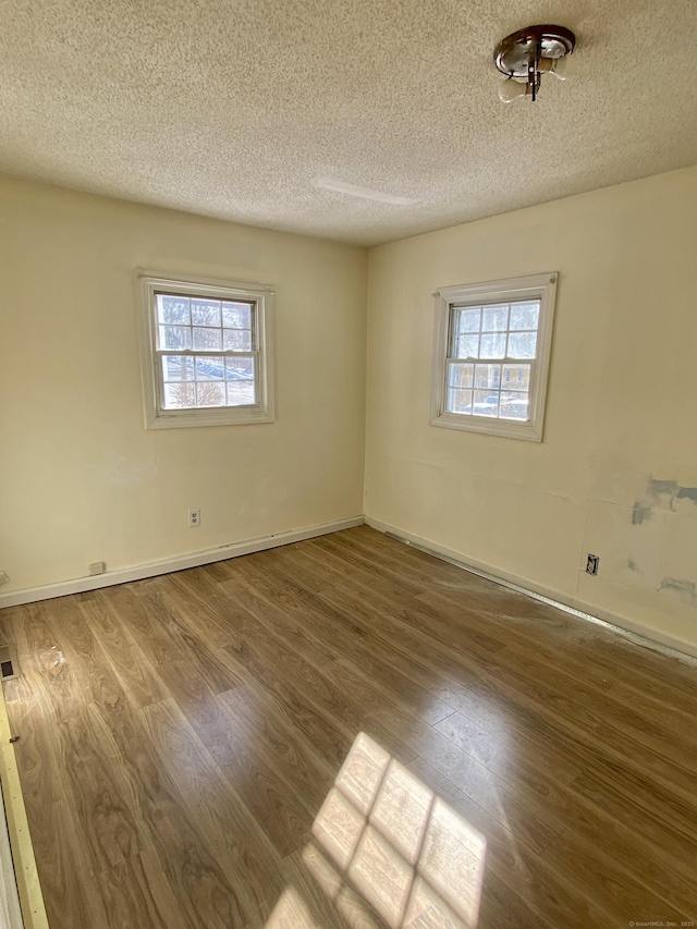 spare room with a healthy amount of sunlight, a textured ceiling, baseboards, and wood finished floors