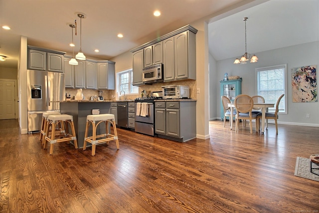 kitchen with gray cabinetry, appliances with stainless steel finishes, decorative backsplash, a center island, and dark wood finished floors