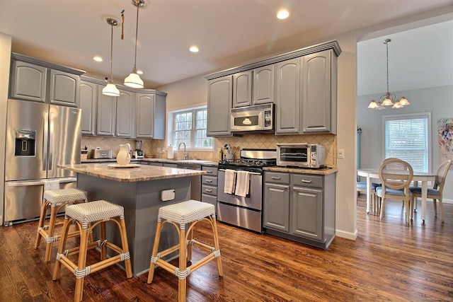 kitchen featuring a toaster, appliances with stainless steel finishes, dark wood-type flooring, a center island, and gray cabinets