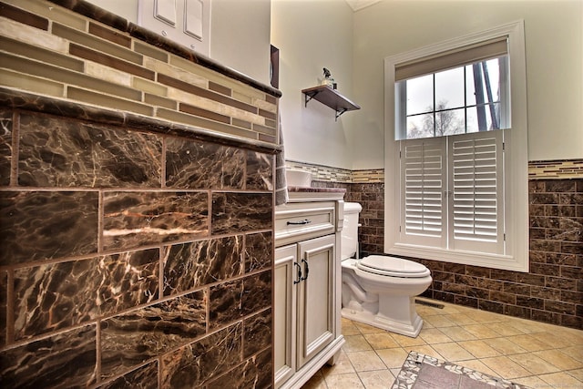 bathroom featuring a wainscoted wall, tile walls, toilet, vanity, and tile patterned flooring