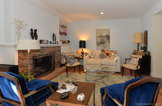 living area featuring vaulted ceiling, a stone fireplace, and wood finished floors