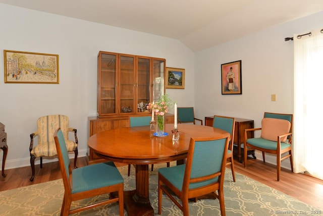 dining room with light wood-style floors, vaulted ceiling, and baseboards