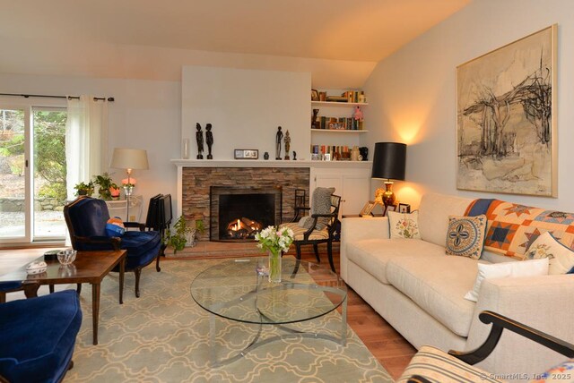 living area with wood finished floors, a stone fireplace, and vaulted ceiling