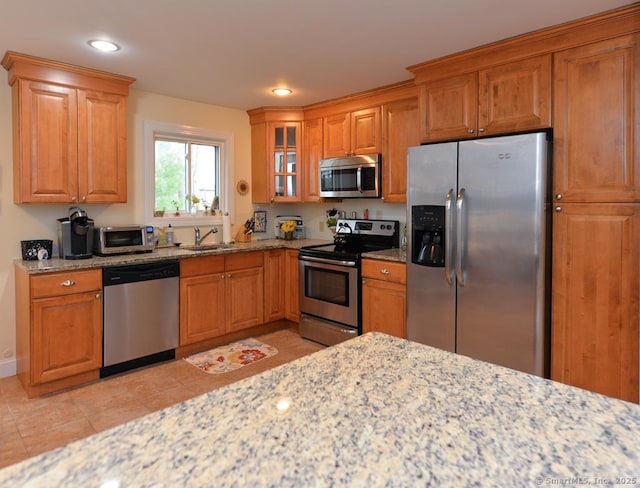 kitchen featuring brown cabinetry, light stone countertops, a sink, and stainless steel appliances
