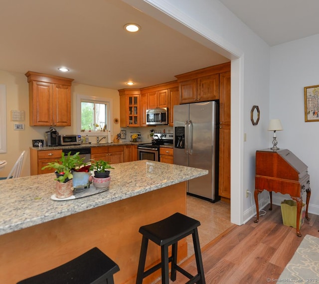 kitchen with brown cabinets, light wood-style floors, glass insert cabinets, a breakfast bar area, and appliances with stainless steel finishes