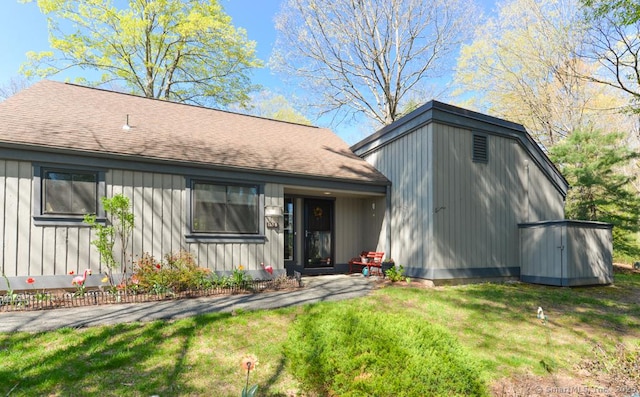 view of front of house with a front yard, board and batten siding, and roof with shingles