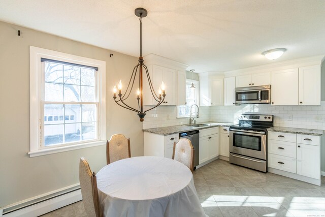 kitchen featuring appliances with stainless steel finishes, decorative light fixtures, light stone countertops, baseboard heating, and white cabinetry