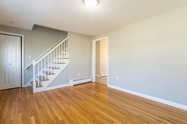 spare room with a baseboard radiator, stairway, a baseboard heating unit, baseboards, and hardwood / wood-style flooring