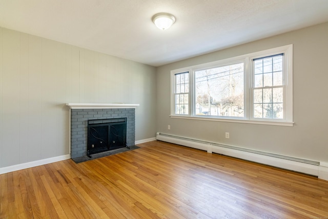 unfurnished living room with a baseboard heating unit, baseboards, a fireplace, and light wood finished floors