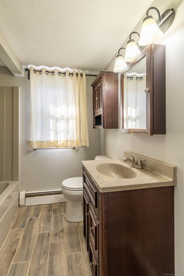 full bath with a bathing tub, wood finished floors, a textured ceiling, vanity, and a baseboard heating unit