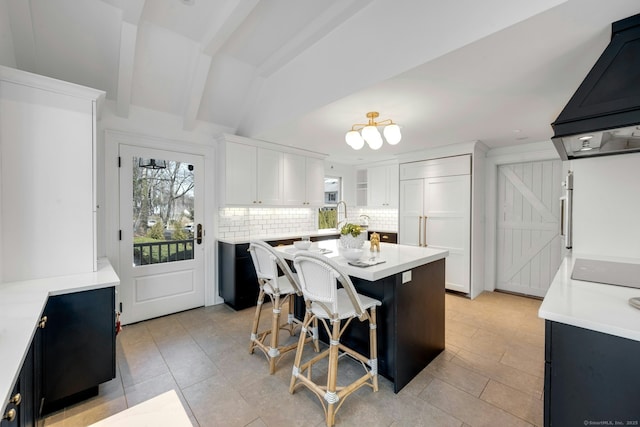 kitchen with vaulted ceiling with beams, light countertops, white cabinets, backsplash, and a center island