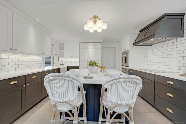 kitchen featuring light tile patterned floors, custom range hood, white cabinets, black electric cooktop, and backsplash