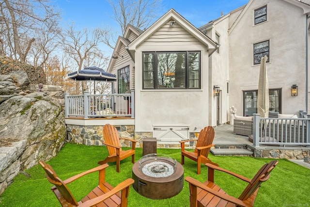 back of property featuring stucco siding, a wooden deck, a lawn, and an outdoor fire pit