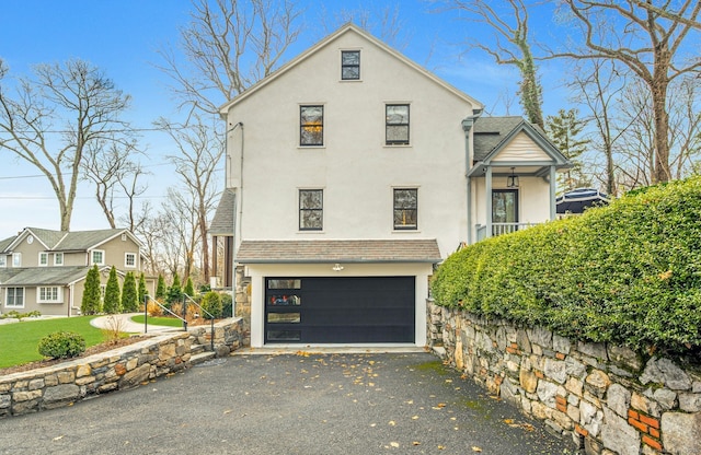 view of front facade featuring aphalt driveway, an attached garage, roof with shingles, and stucco siding