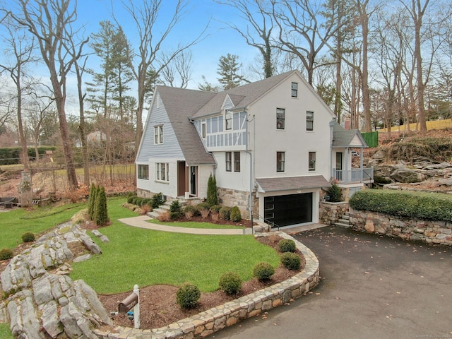 view of front of house featuring a front yard, stucco siding, a balcony, stone siding, and driveway