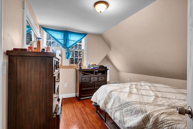 bedroom with vaulted ceiling, wood finished floors, and baseboards