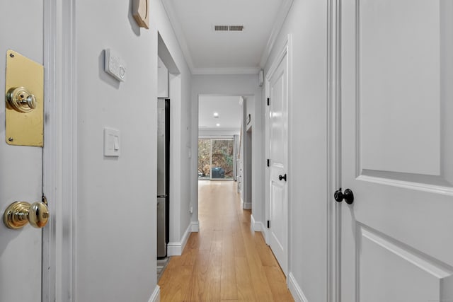 hallway featuring baseboards, ornamental molding, visible vents, and light wood-style floors