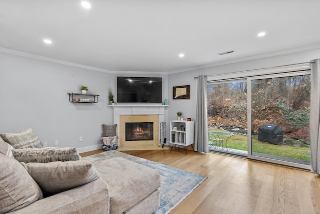 living area featuring ornamental molding, visible vents, a tiled fireplace, and wood finished floors