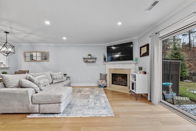 living room featuring a fireplace with flush hearth, visible vents, wood finished floors, and ornamental molding