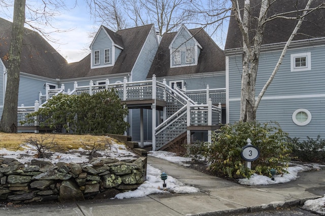 view of front of house featuring roof with shingles, stairway, and a wooden deck