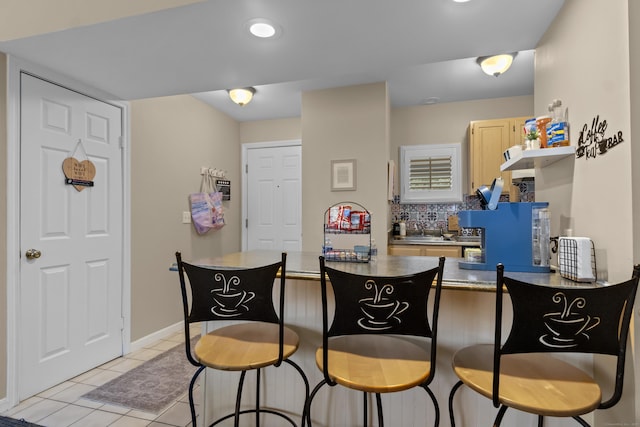 kitchen with decorative backsplash, a peninsula, a breakfast bar area, and light tile patterned floors