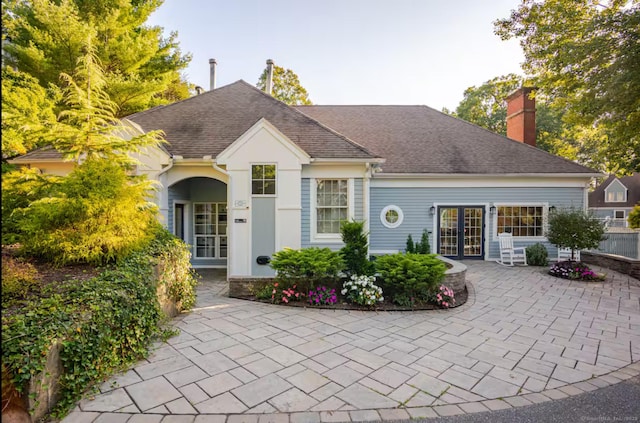 view of front of property with a shingled roof, fence, french doors, a chimney, and a patio area