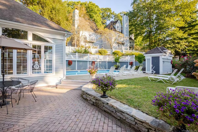 view of patio / terrace featuring an outdoor pool, fence, an outdoor structure, and a storage unit