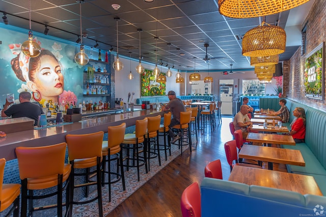 bar with a bar, a paneled ceiling, track lighting, and wood finished floors