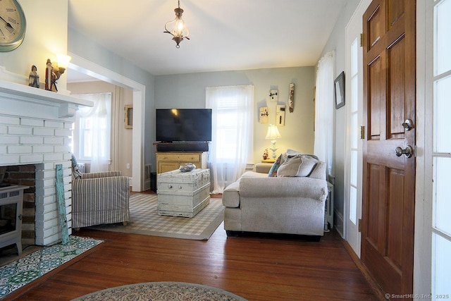 living area with dark wood-type flooring, a brick fireplace, and a healthy amount of sunlight