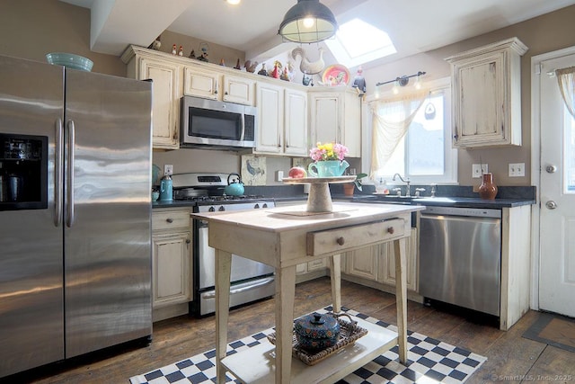 kitchen with dark countertops, a skylight, appliances with stainless steel finishes, and dark wood-type flooring