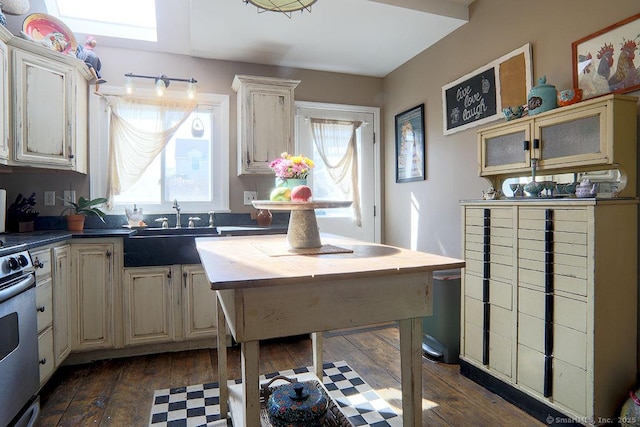 kitchen with a sink, stainless steel range with electric stovetop, cream cabinetry, dark wood finished floors, and glass insert cabinets