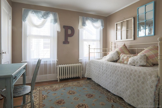 bedroom featuring multiple windows, crown molding, radiator heating unit, and wood finished floors