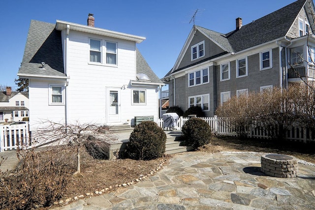 rear view of house featuring a fire pit, roof with shingles, fence, and a chimney