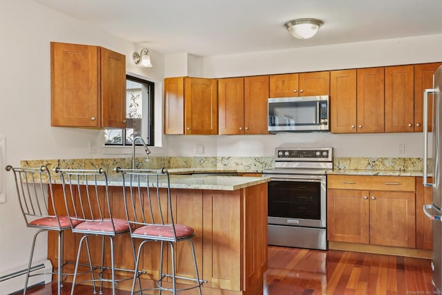 kitchen featuring appliances with stainless steel finishes, brown cabinetry, a baseboard heating unit, and a kitchen breakfast bar