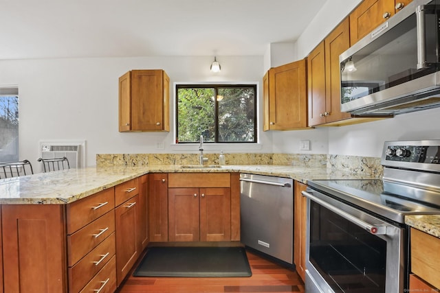 kitchen with dark wood finished floors, stainless steel appliances, brown cabinetry, a sink, and a peninsula