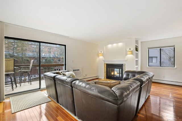 living area with hardwood / wood-style flooring, a baseboard radiator, built in shelves, and a glass covered fireplace