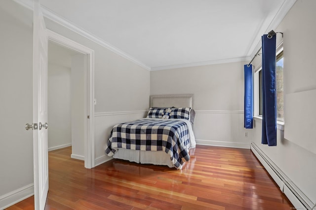 bedroom featuring a baseboard heating unit, hardwood / wood-style floors, wainscoting, and crown molding