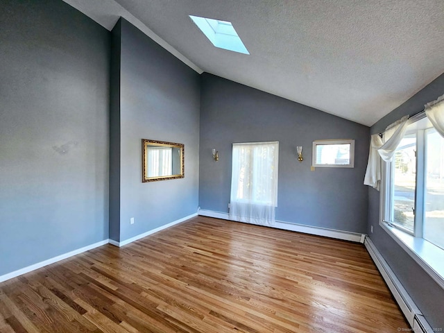 interior space with a baseboard heating unit, vaulted ceiling with skylight, wood finished floors, and baseboards