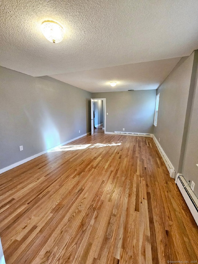 empty room featuring baseboards, a textured ceiling, baseboard heating, and wood finished floors