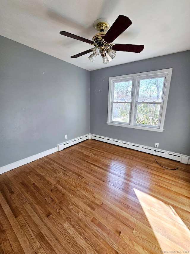 spare room with a baseboard heating unit, a ceiling fan, baseboards, and wood finished floors