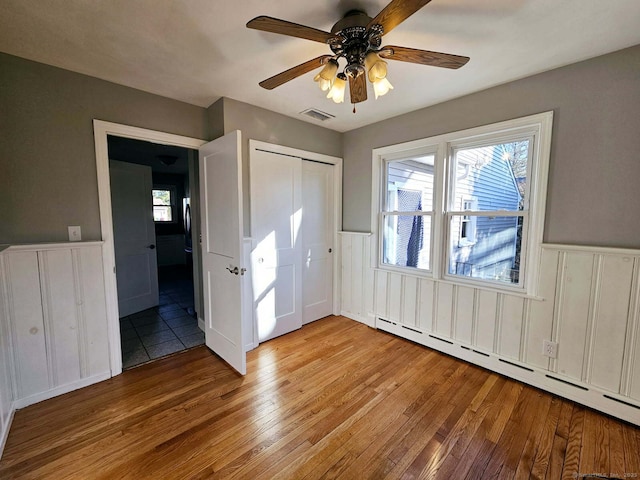 unfurnished bedroom with light wood-style floors, visible vents, a baseboard heating unit, and a wainscoted wall