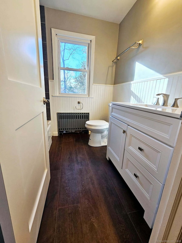 full bath featuring toilet, vanity, wainscoting, radiator, and hardwood / wood-style floors